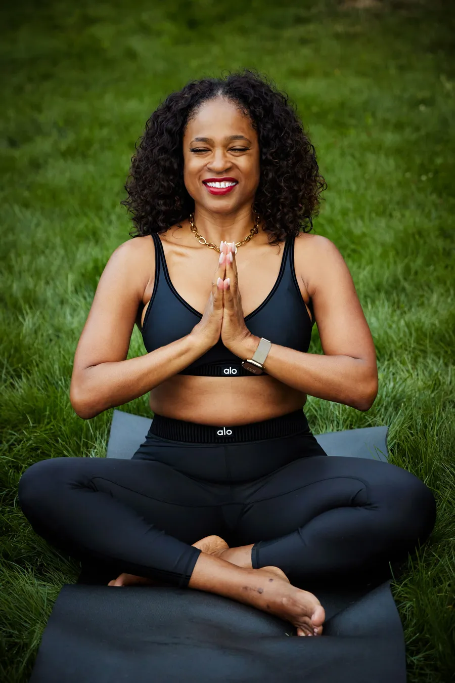 Ardie seated in lotus pose with hands in prayer, smiling, overlooking the Columbia River Gorge