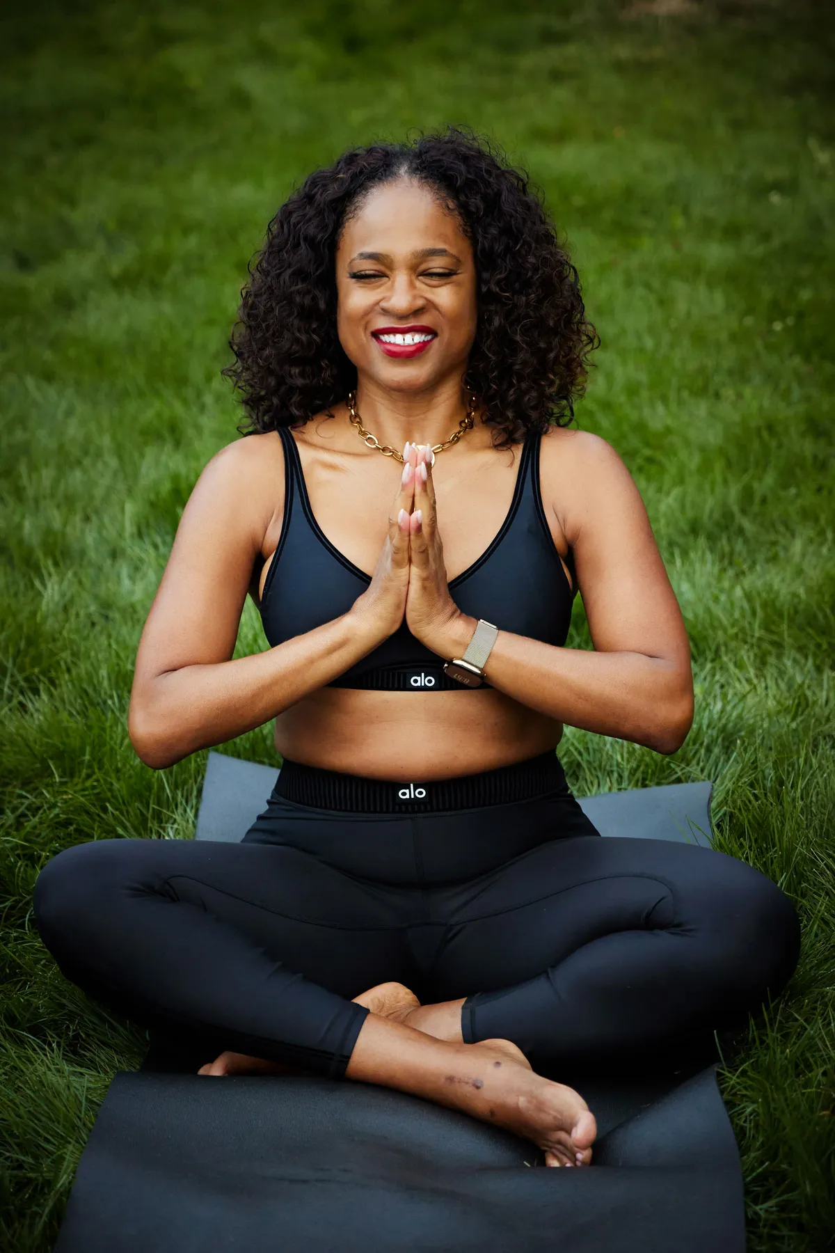 Ardie seated in lotus pose with hands in prayer, smiling, overlooking the Columbia River Gorge