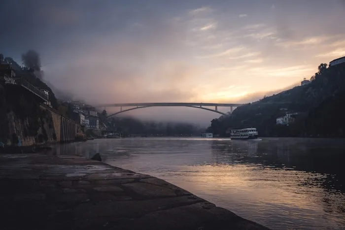 A misty river at dawn, with an arch bridge in the distance